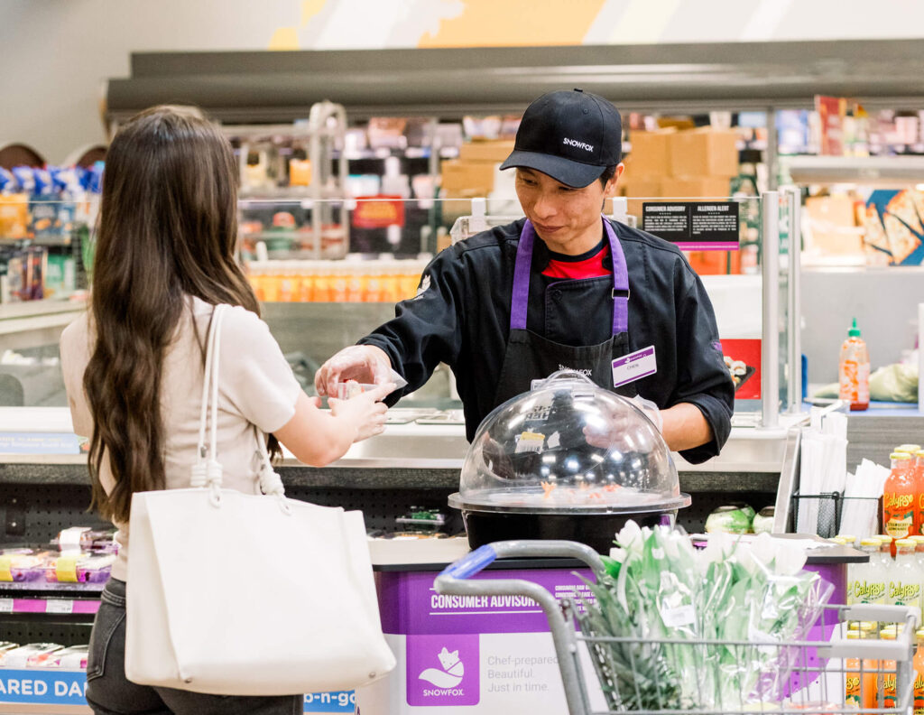 A worker handing sushi to a customer in a grocery store
